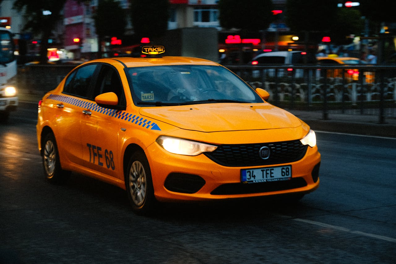 Yellow taxi driving on a busy city street at dusk with blurred lights in the background.